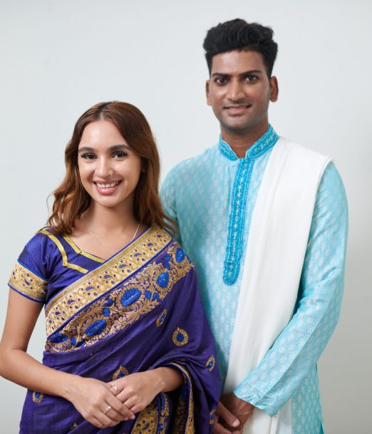 Portrait of happy Indian man and woman in traditional clothes standing against white wall